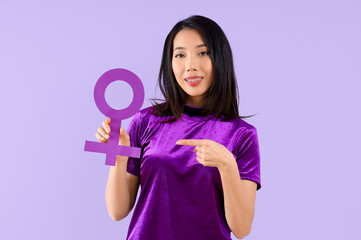 Young Asian woman pointing at gender symbol on lilac background