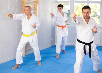 Adult man in kimono trains karate techniques in group in studio