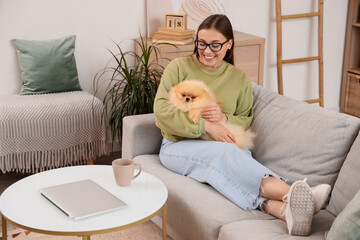 Young woman with cute Pomeranian dog resting on sofa at home