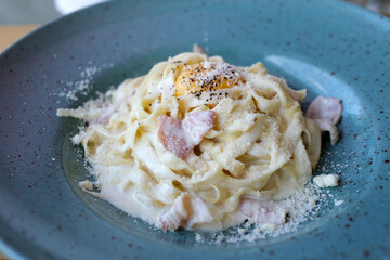 Linguini pasta with carbonara sauce on a dark background. Carbonara sauce made of bacon, parmesan, egg, cream and pepper. Italian food.