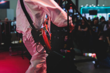 Concert view of an electric guitar player with vocalist and rock band performing in a club, male musician guitarist on stage with audience in a crowded concert hall arena, hands on a guitar