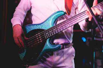 Obraz na płótnie Canvas Concert view of a musician, electric bass guitar player with during band performing rock music, bassist player on stage