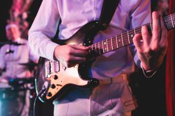 Obraz na płótnie Canvas Concert view of an electric guitar player with vocalist and rock band performing in a club, male musician guitarist on stage with audience in a crowded concert hall arena