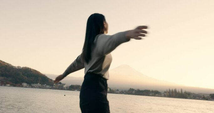 Japanese woman, freedom and happiness outdoor, lake or ocean with travel, holiday and mindfulness in nature. Wellness, adventure and care free at beach in Japan, smile with spinning and positivity