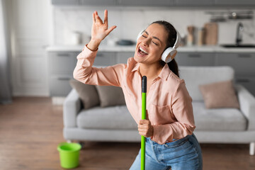 Delighted young woman singing with mop while doing housework