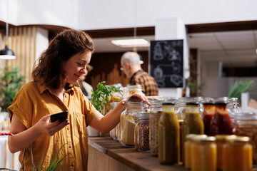 Green living woman on a diet using smartphone to make sure zero waste supermarket food is good for...