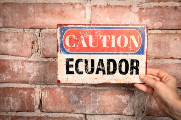 Fototapeta na wymiar Ecuador. Caution sign in a woman's hand on a brick background