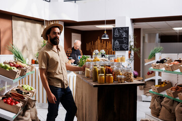 Portrait of cheerful man looking for farm grown vegetables in sustainable zero waste store. Hipster client does grocery shopping, buying chemicals free food in local neighborhood store