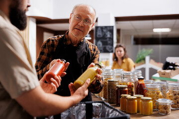 Zero waste shop clerk providing ecological bio groceries to elderly delivery man. Older man...