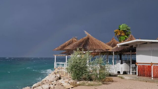 Slow motion colourful rainbow above the disquiet sea surface. Continuously changing weather conditions, light and shadow. Powerful waves crashing the coast after Storm Ciar&aacute;n smashed into Krk Island.