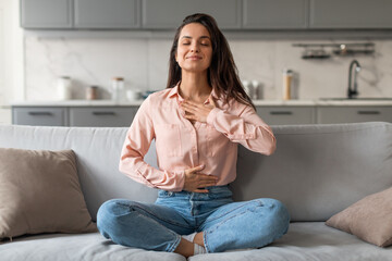 Relaxed young woman meditating on sofa at home