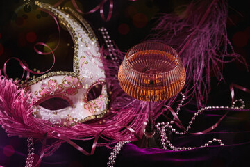 Masquerade ball holiday background. Glass of rose champagne, Venetian carnival mask and feathers on...