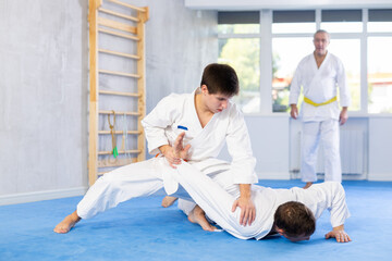 Two men practice grabbing and throwing sports mats during judo training under the guidance of an...