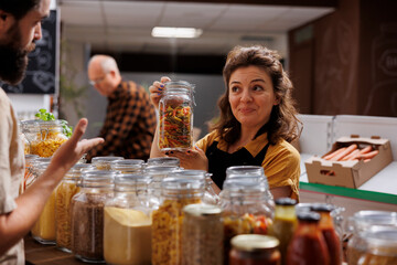 Seller offering customer information about product in environmentally responsible zero waste store. Storekeeper helping client looking for homemade pasta in local neighborhood shop