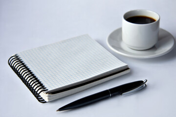 Close-up of a blank notepad with a black pen and a cup of coffee on a white background.