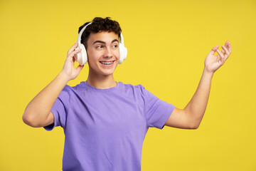 Portrait positive teenage boy wearing purple t shirt looking away listening to music in headphones