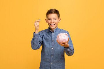 Cheerful teen boy holding coin and pink piggy bank - obrazy, fototapety, plakaty