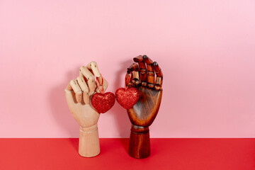 St Valentine's still life with brown and white wooden mannequin hands holding sparkling heart on pink and red background
