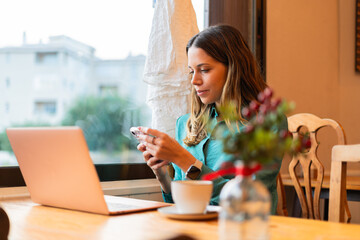 Young woman scrolls through her phone at a vintage coffee place, balancing work and connectivity