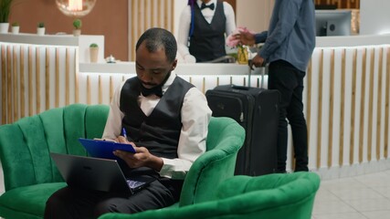 Tourism industry employee. Bellboy entering data document forms on papers in lounge area, hotel...