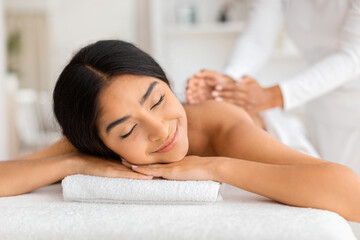 Fototapeta na wymiar Joyful young indian woman receiving relaxing back massage