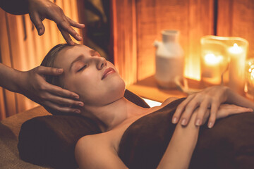 Caucasian woman enjoying relaxing anti-stress head massage and pampering facial beauty skin recreation leisure in warm candle lighting ambient salon spa in luxury resort or hotel. Quiescent - obrazy, fototapety, plakaty