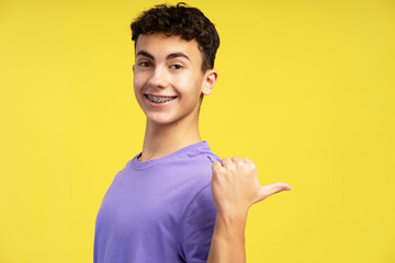 Portrait of smiling boy wearing casual purple t shirt looking at camera showing finger on copy space