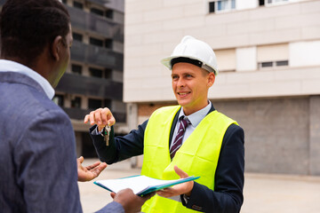 Young positive contractor hands an african-american man customer the keys to an apartment in a new building