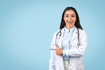Cheerful woman doctor pointing to the side, blue background