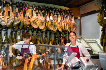 Fototapeta na wymiar Young couple work together in butcher shop - they cut the traditional Spanish jamon