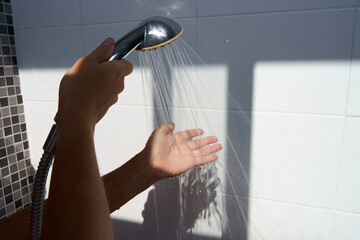 Female hand touching water pouring from a rain shower head, checking water temperature.