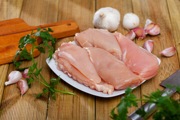 Raw boneless chicken breast on wooden surface with seasonings. Dietary cooking ingredient