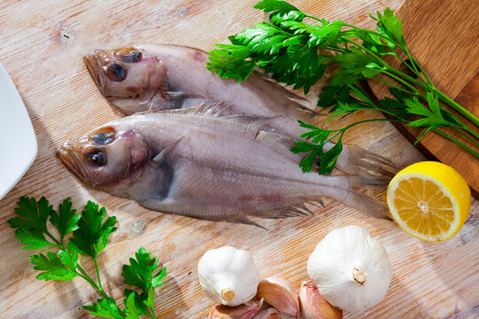 Two whole fresh Mediterranean megrims on wooden surface with seasonings prepared for cooking