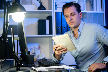 Working businessman focusing notebook at neon workplace, planning online business on paperwork...