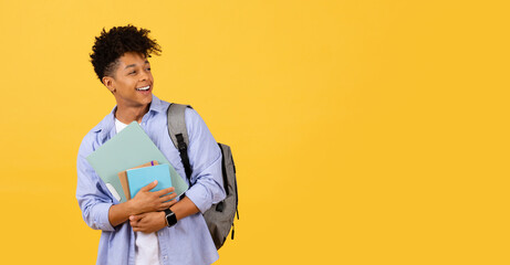 Joyful black student with books and backpack on yellow
