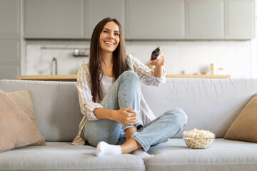 Delighted female with bowl of popcorn at home watching her favorite shows - obrazy, fototapety, plakaty