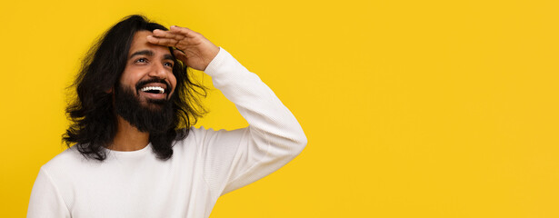 Curious indian man looking at copy space, yellow background