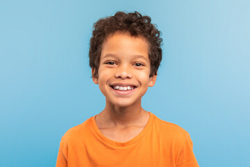 Happy boy in orange shirt with big smile, blue background
