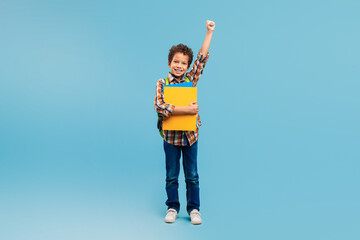 Exuberant schoolboy with fist up, holding folder, ready for school