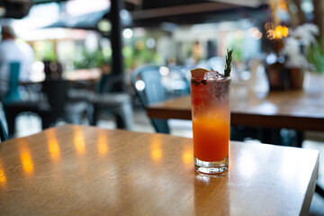 delicious cocktail garnished with watermelon slice, rosemary, and orange juice in a tall glass with ice at bar during the daytime