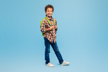 Smiling boy with backpack in plaid shirt, blue background © Prostock-studio