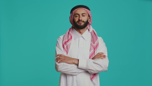 Man in religious thobe and kufiyah, being pleased indicating muslim cultural identity and national tradition. Middle eastern person dressed in robe and checkered headscarf.