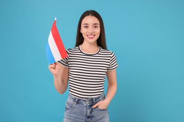 Young woman holding flag of Netherlands on light blue background