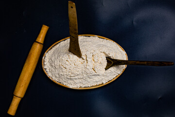 Wheat flour on a wooden plate and a wooden roller