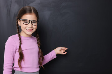 Cute schoolgirl in glasses near chalkboard, space for text