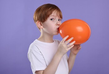 Fototapeta na wymiar Boy inflating orange balloon on violet background
