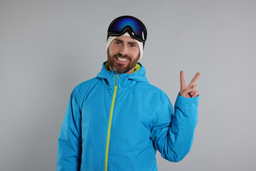 Winter sports. Happy man in ski suit and goggles showing V-sign on gray background