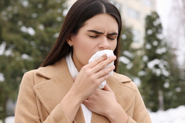 Woman in coat coughing outdoors. Cold symptoms
