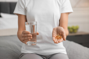 Woman with pills and glass of water on bed in room. Weight loss