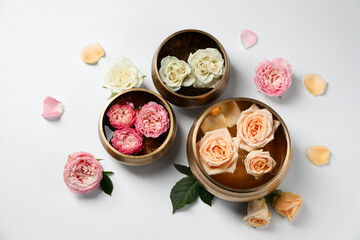 Tibetan singing bowls with water and different beautiful rose flowers on white background, flat lay